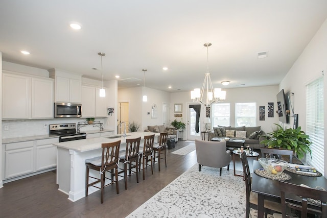 kitchen featuring hanging light fixtures, stainless steel appliances, an island with sink, and dark wood-type flooring