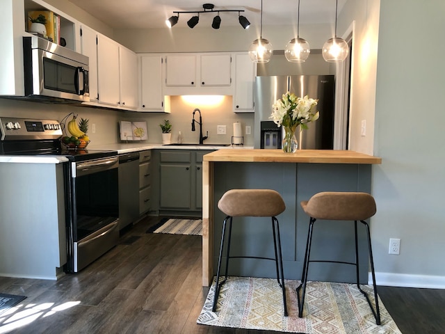 kitchen featuring appliances with stainless steel finishes, dark wood-type flooring, sink, white cabinets, and hanging light fixtures