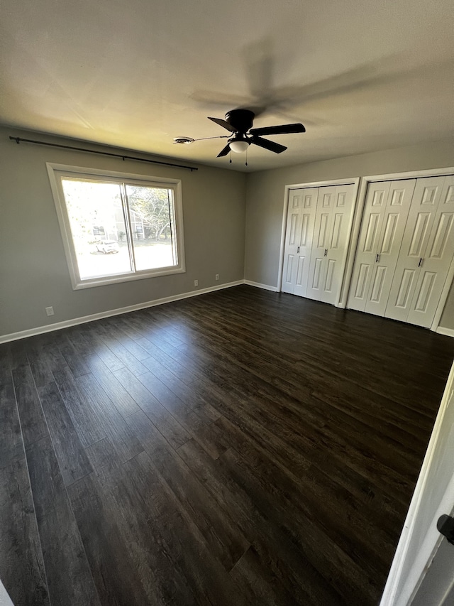 unfurnished bedroom featuring ceiling fan, dark wood-type flooring, and two closets