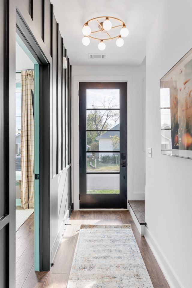 doorway to outside with light wood-type flooring and an inviting chandelier