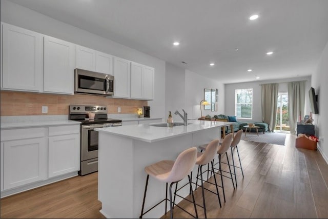 kitchen with a center island with sink, sink, light wood-type flooring, white cabinetry, and stainless steel appliances