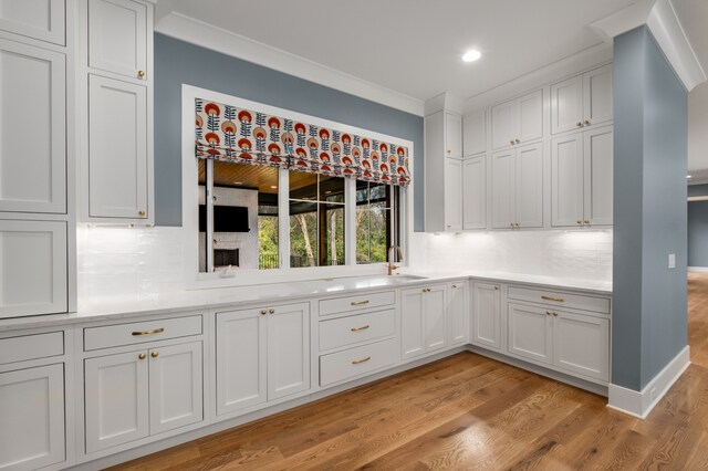 kitchen featuring decorative backsplash, white cabinets, light hardwood / wood-style flooring, and crown molding