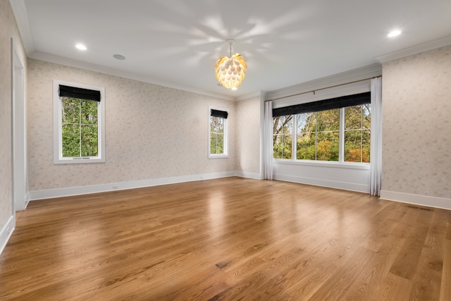 spare room featuring a wealth of natural light, crown molding, light hardwood / wood-style floors, and a notable chandelier