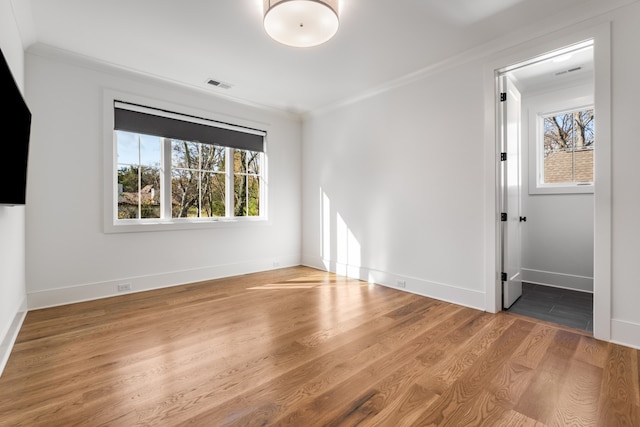 empty room featuring a wealth of natural light, crown molding, and hardwood / wood-style flooring