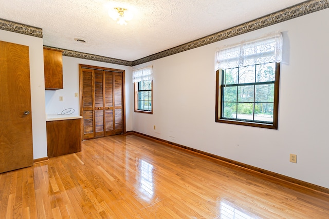 unfurnished bedroom featuring multiple windows, light hardwood / wood-style floors, and a textured ceiling