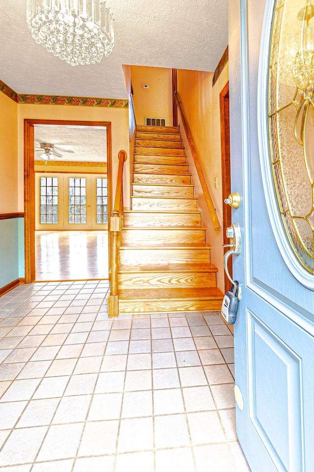 tiled entryway with a textured ceiling and ceiling fan with notable chandelier