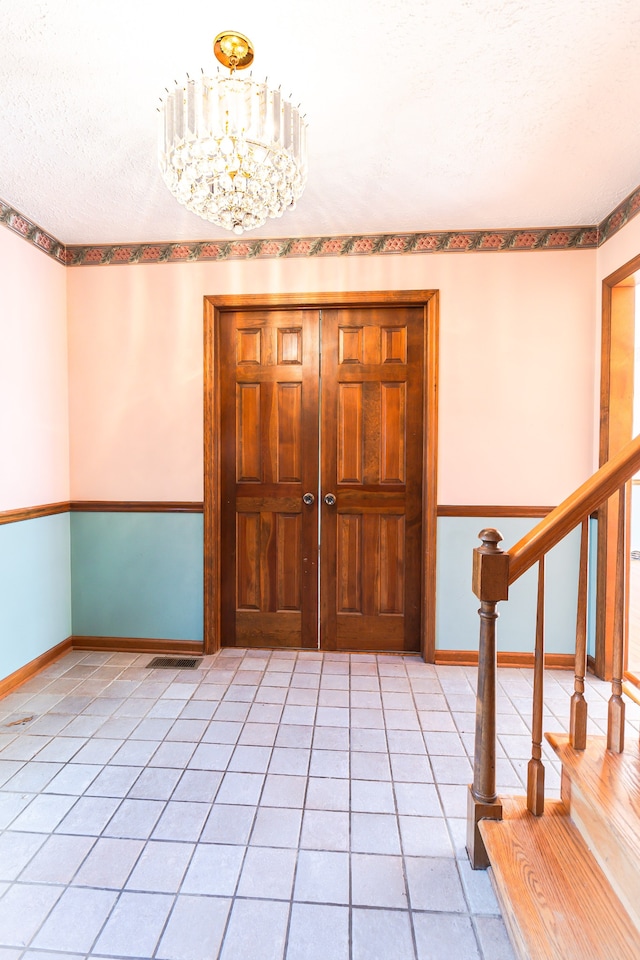 foyer featuring light tile patterned floors, a textured ceiling, and an inviting chandelier