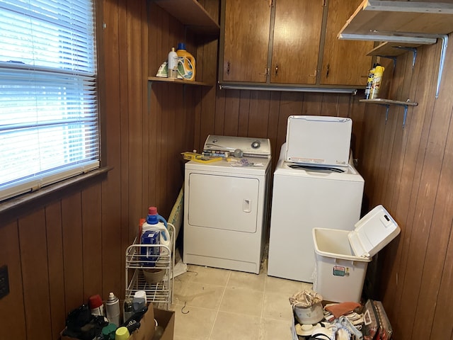 laundry area featuring washer and clothes dryer, light tile patterned flooring, cabinets, and wooden walls