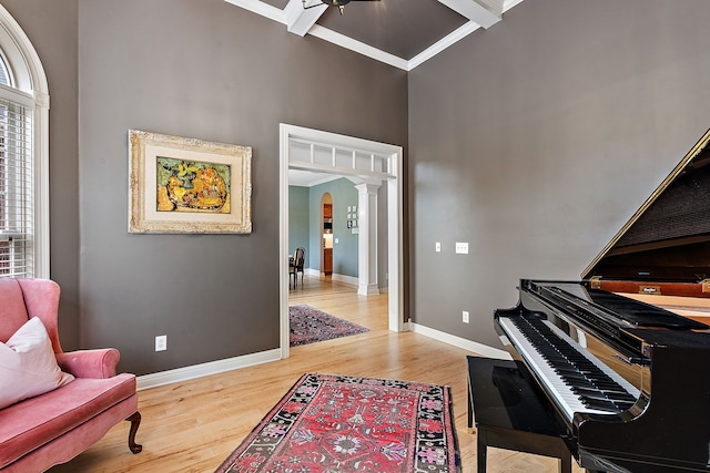 sitting room with beam ceiling, ornate columns, a towering ceiling, wood-type flooring, and ornamental molding