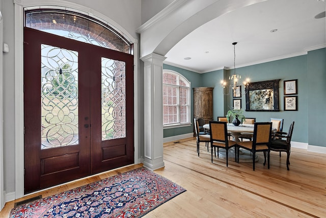 foyer entrance featuring french doors, an inviting chandelier, decorative columns, crown molding, and light hardwood / wood-style floors