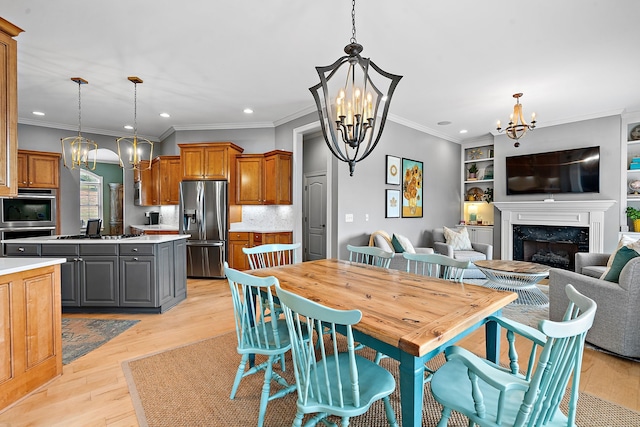 dining room with built in shelves, crown molding, an inviting chandelier, light hardwood / wood-style flooring, and a premium fireplace