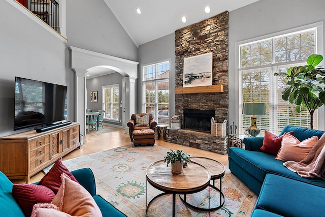 living room featuring decorative columns, high vaulted ceiling, a stone fireplace, and light hardwood / wood-style floors