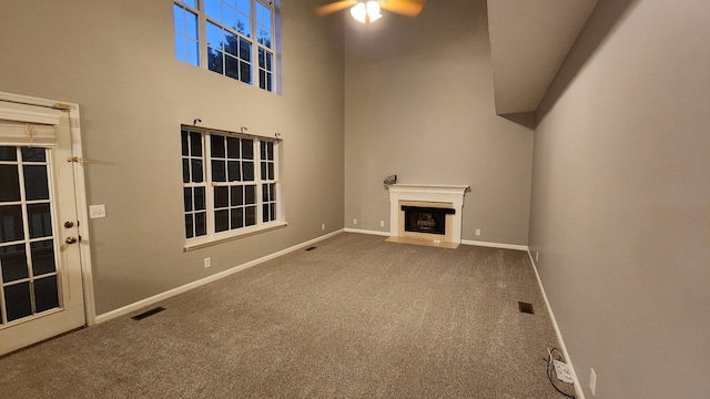 unfurnished living room with carpet flooring, a towering ceiling, and ceiling fan