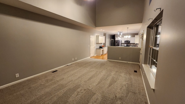 unfurnished living room with a towering ceiling, light colored carpet, and an inviting chandelier