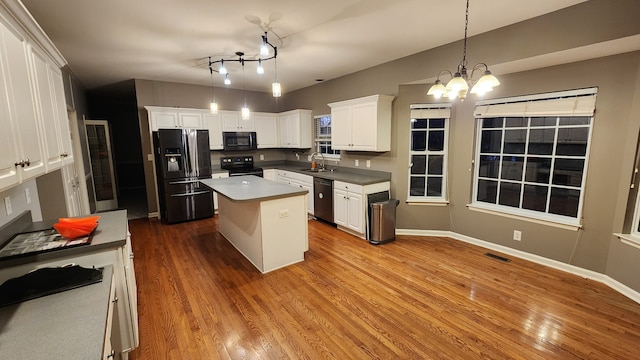 kitchen featuring white cabinets, a center island, decorative light fixtures, and black appliances