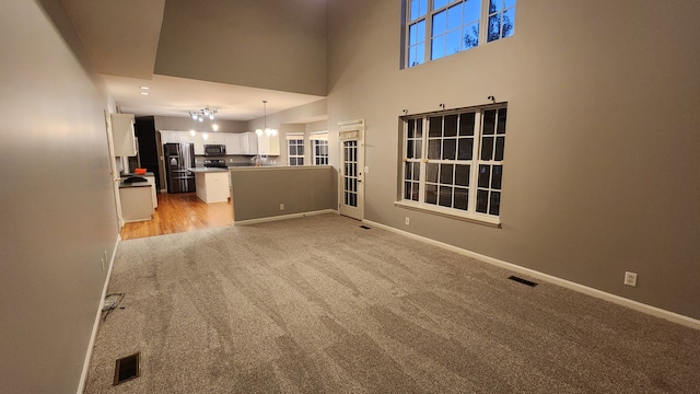 unfurnished living room featuring light colored carpet, a chandelier, and a high ceiling