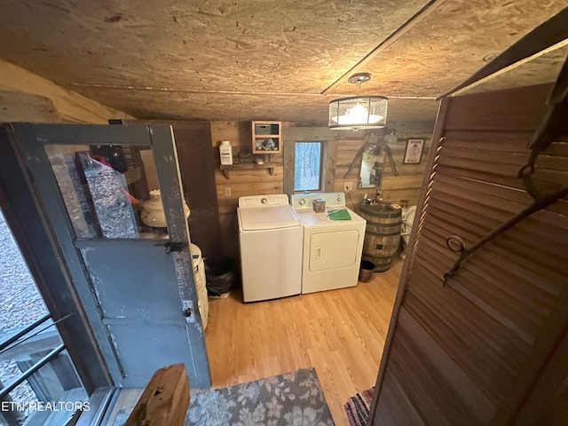 clothes washing area featuring wooden walls, washer and dryer, and light wood-type flooring