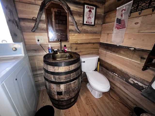 bathroom featuring wooden walls, washer / clothes dryer, sink, hardwood / wood-style flooring, and toilet