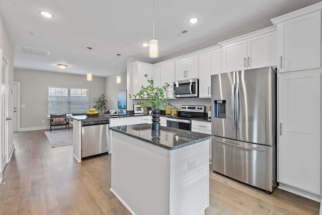 kitchen featuring stainless steel appliances, white cabinets, a center island, light hardwood / wood-style floors, and hanging light fixtures