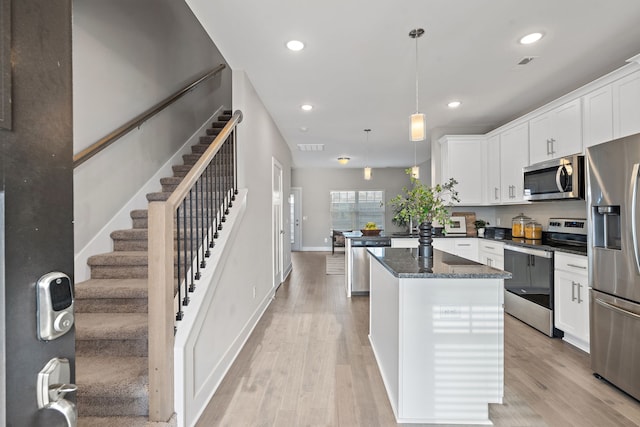 kitchen with a center island, light wood-type flooring, decorative light fixtures, white cabinetry, and stainless steel appliances