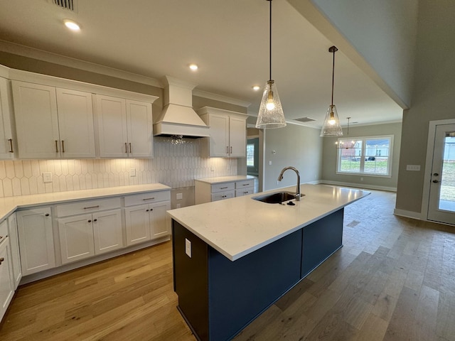 kitchen with white cabinets, a sink, custom exhaust hood, light wood-type flooring, and backsplash