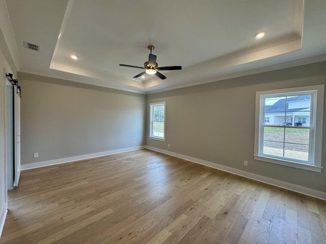 unfurnished room with light wood finished floors, a barn door, visible vents, a tray ceiling, and crown molding