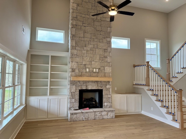 unfurnished living room with a stone fireplace, light wood finished floors, stairway, and a healthy amount of sunlight