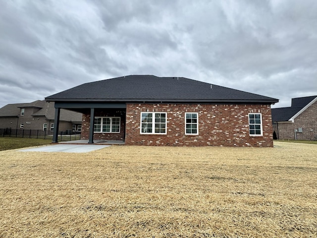 back of house with brick siding, fence, roof with shingles, a lawn, and a patio area