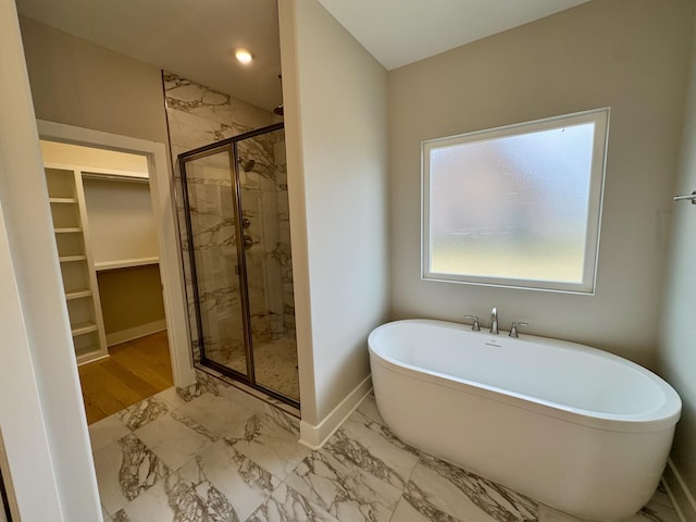 bathroom featuring baseboards, marble finish floor, a walk in closet, a freestanding tub, and a shower stall