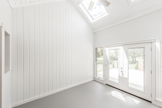 doorway with ceiling fan, lofted ceiling with skylight, wooden walls, and concrete floors