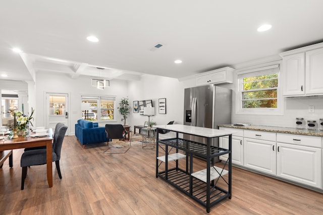 kitchen with white cabinetry, beam ceiling, light hardwood / wood-style floors, light stone counters, and stainless steel fridge with ice dispenser