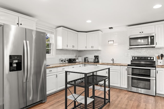 kitchen featuring appliances with stainless steel finishes, light wood-type flooring, sink, pendant lighting, and white cabinets