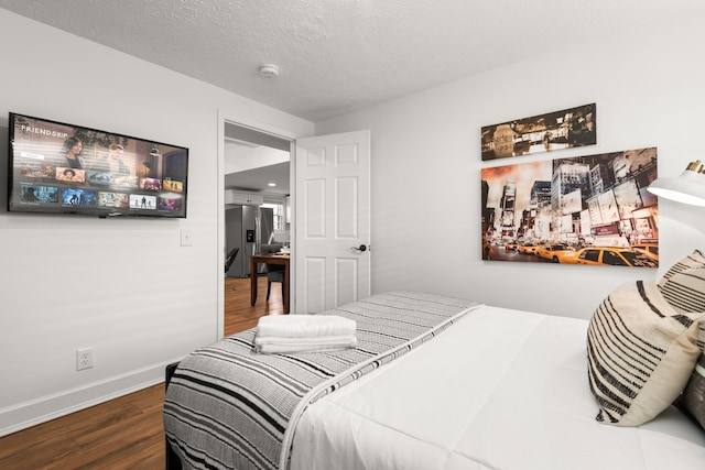 bedroom featuring stainless steel fridge, dark wood-type flooring, and a textured ceiling