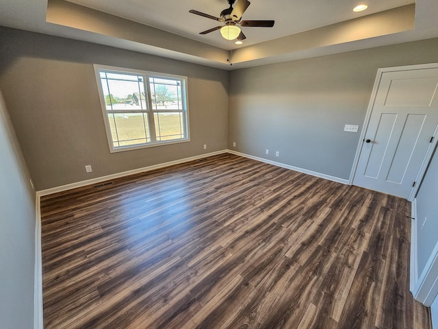 unfurnished room featuring a tray ceiling, dark wood-type flooring, and ceiling fan