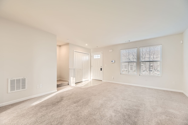 empty room featuring baseboards, stairs, visible vents, and light colored carpet