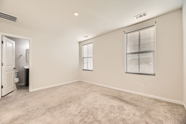 unfurnished bedroom with connected bathroom and light carpet