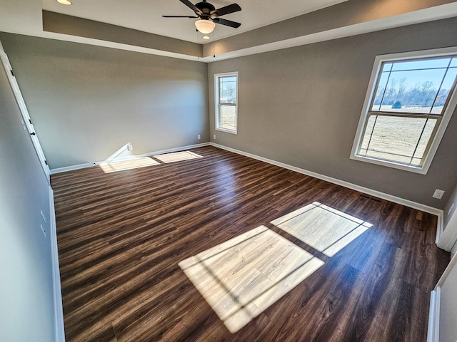 empty room with ceiling fan, a tray ceiling, dark hardwood / wood-style flooring, and a wealth of natural light