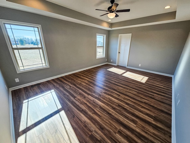 empty room with a raised ceiling, ceiling fan, and dark hardwood / wood-style flooring