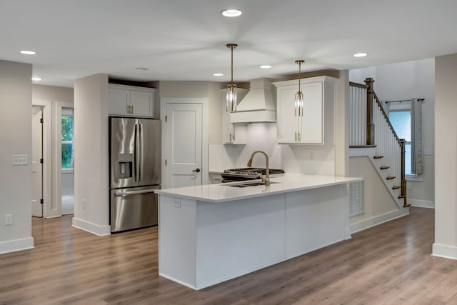 kitchen with stainless steel appliances, a sink, wood finished floors, light countertops, and custom exhaust hood