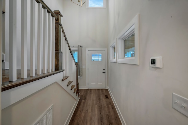 doorway to outside with dark wood finished floors, visible vents, a towering ceiling, baseboards, and stairs