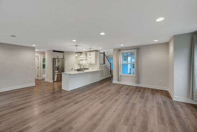 unfurnished living room with recessed lighting, a sink, baseboards, and wood finished floors