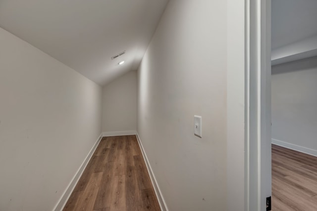 corridor with vaulted ceiling, wood finished floors, visible vents, and baseboards