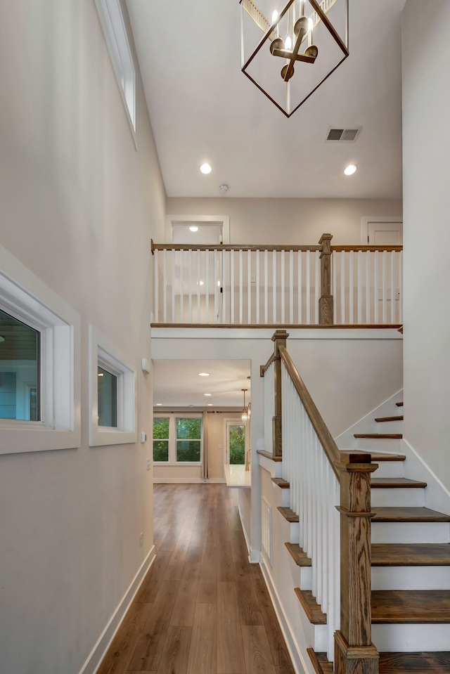 stairway with visible vents, a towering ceiling, hardwood / wood-style floors, a chandelier, and baseboards