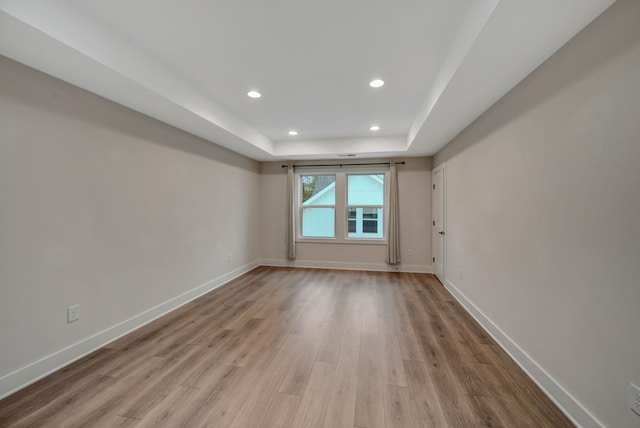 empty room featuring baseboards, a raised ceiling, wood finished floors, and recessed lighting