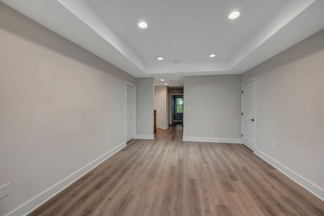 empty room with light wood-style floors, recessed lighting, a raised ceiling, and baseboards