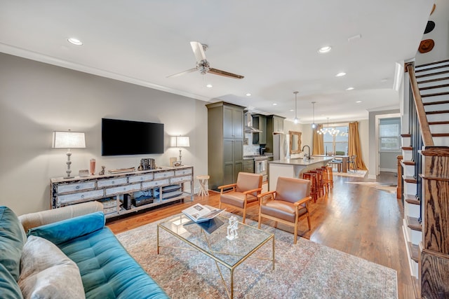 living room featuring ceiling fan with notable chandelier, light hardwood / wood-style floors, crown molding, and sink