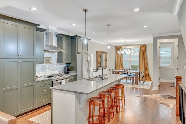 kitchen featuring a kitchen bar, appliances with stainless steel finishes, sink, wall chimney range hood, and hanging light fixtures