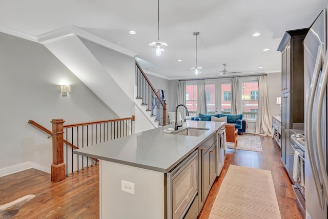 kitchen featuring sink, light hardwood / wood-style flooring, pendant lighting, a center island with sink, and ornamental molding