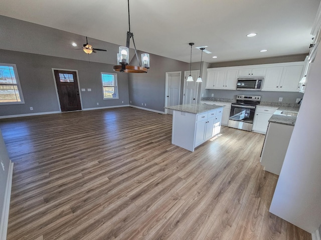 kitchen with light wood-type flooring, appliances with stainless steel finishes, a kitchen island, pendant lighting, and white cabinets