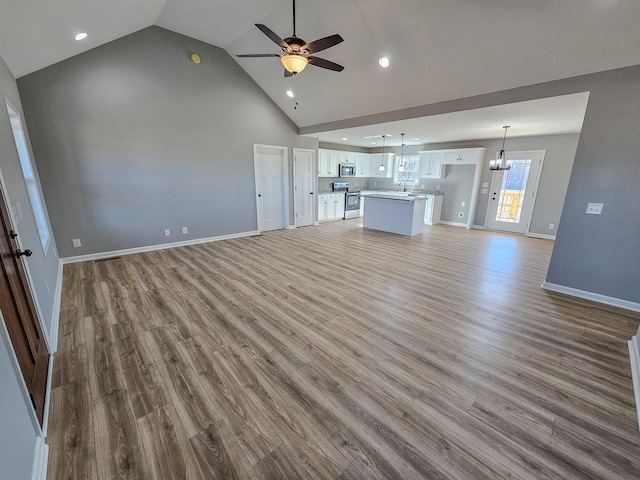 unfurnished living room featuring sink, ceiling fan with notable chandelier, light hardwood / wood-style flooring, and high vaulted ceiling